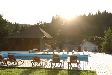 Photo of Outdoor swimming pool, sunbeds and houses near forest on sunny day