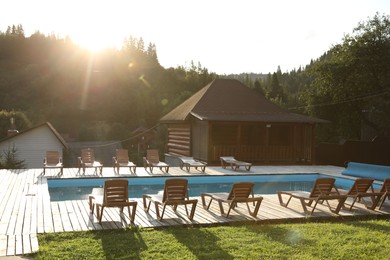 Photo of Outdoor swimming pool, sunbeds and houses near forest on sunny day