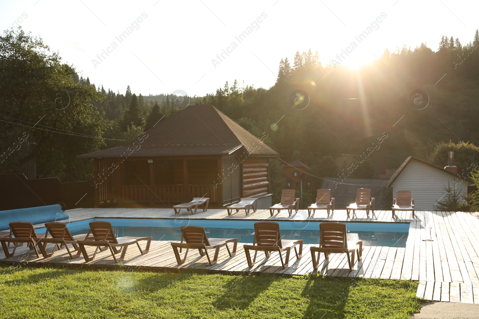 Photo of Outdoor swimming pool, sunbeds and houses near forest on sunny day