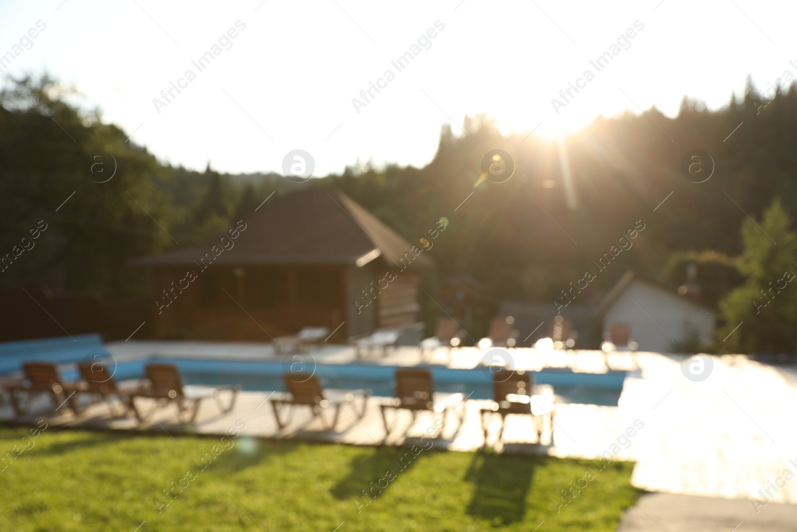 Photo of Outdoor swimming pool, sunbeds and houses near forest on sunny day, blurred view