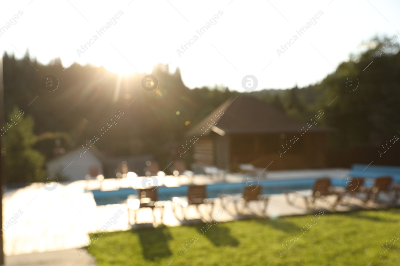 Photo of Outdoor swimming pool, sunbeds and houses near forest on sunny day, blurred view