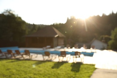 Photo of Outdoor swimming pool, sunbeds and houses near forest on sunny day, blurred view