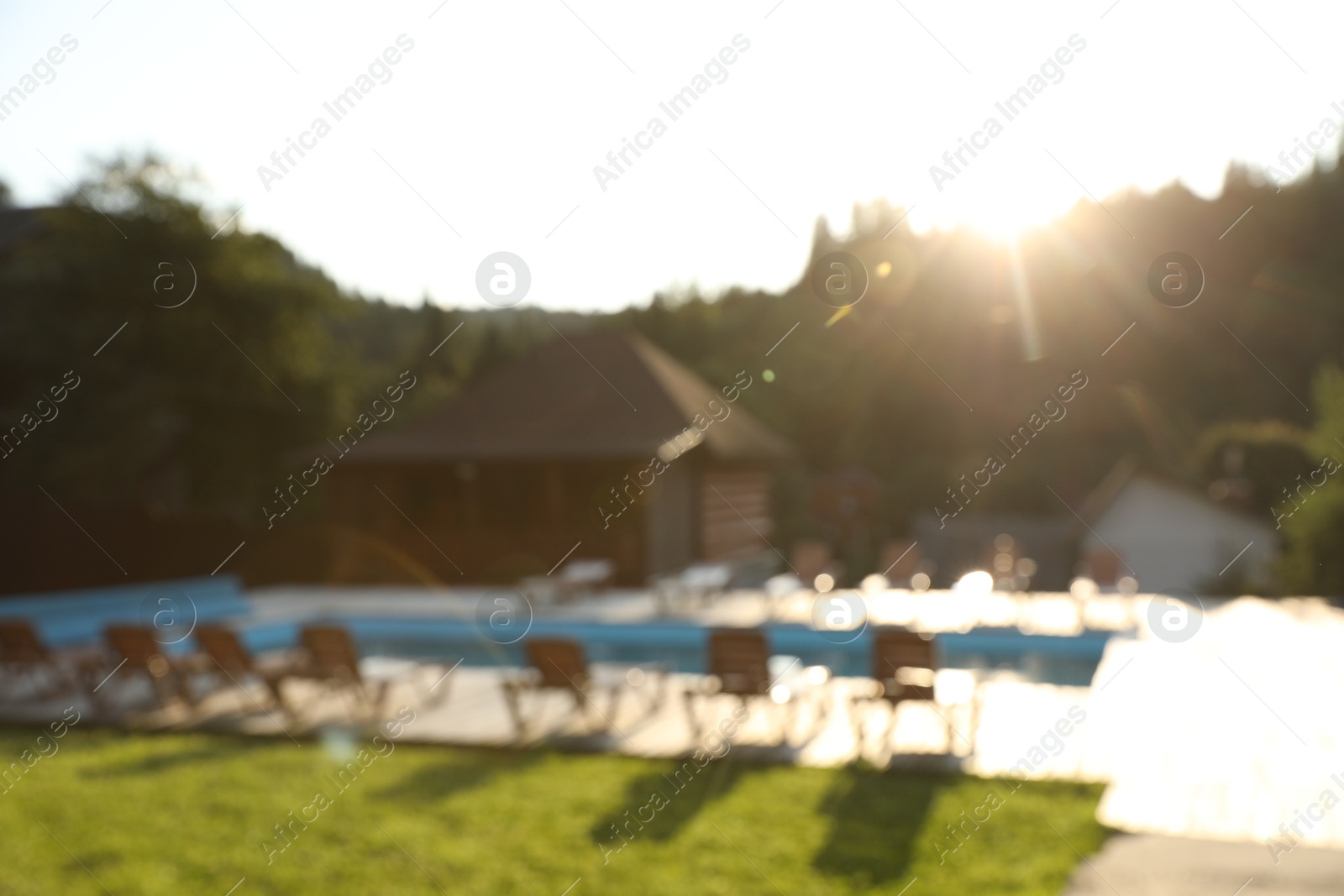 Photo of Outdoor swimming pool, sunbeds and houses near forest on sunny day, blurred view