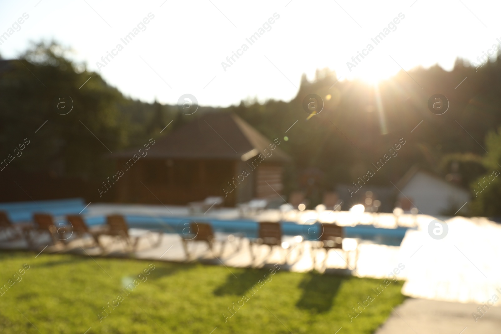 Photo of Outdoor swimming pool, sunbeds and houses near forest on sunny day, blurred view