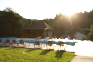 Photo of Outdoor swimming pool, sunbeds and houses near forest on sunny day, blurred view