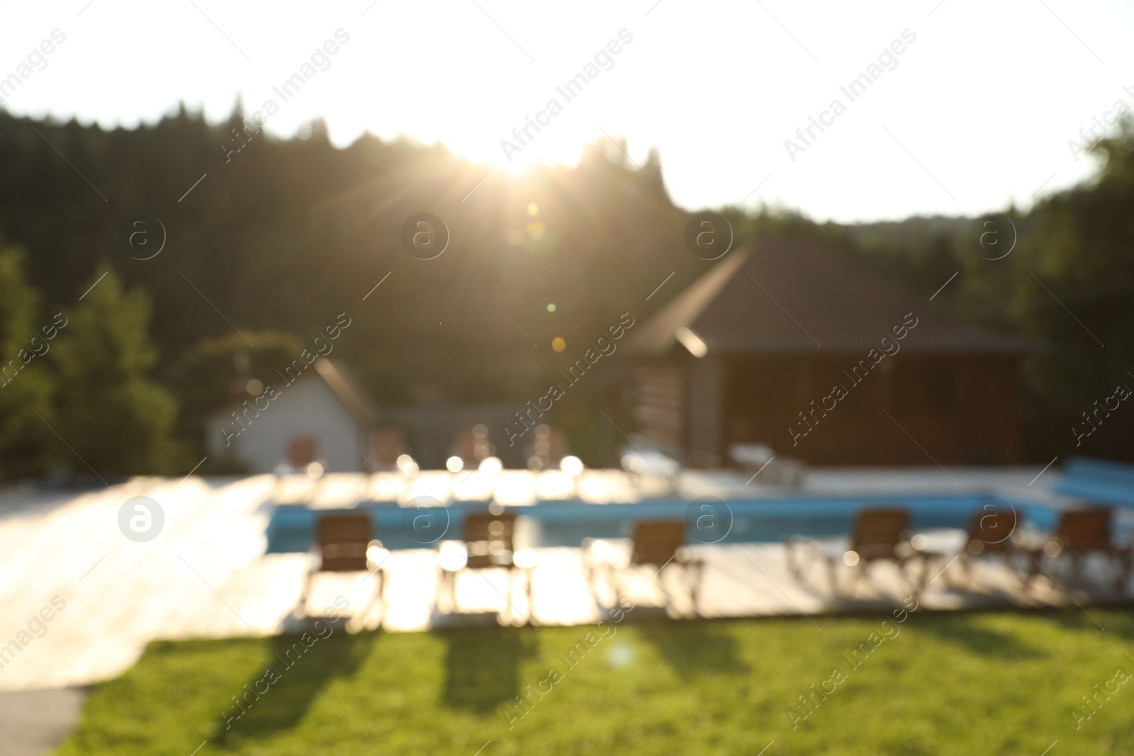 Photo of Outdoor swimming pool, sunbeds and houses near forest on sunny day, blurred view