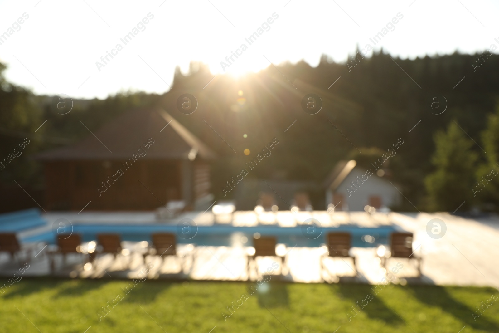 Photo of Outdoor swimming pool, sunbeds and houses near forest on sunny day, blurred view