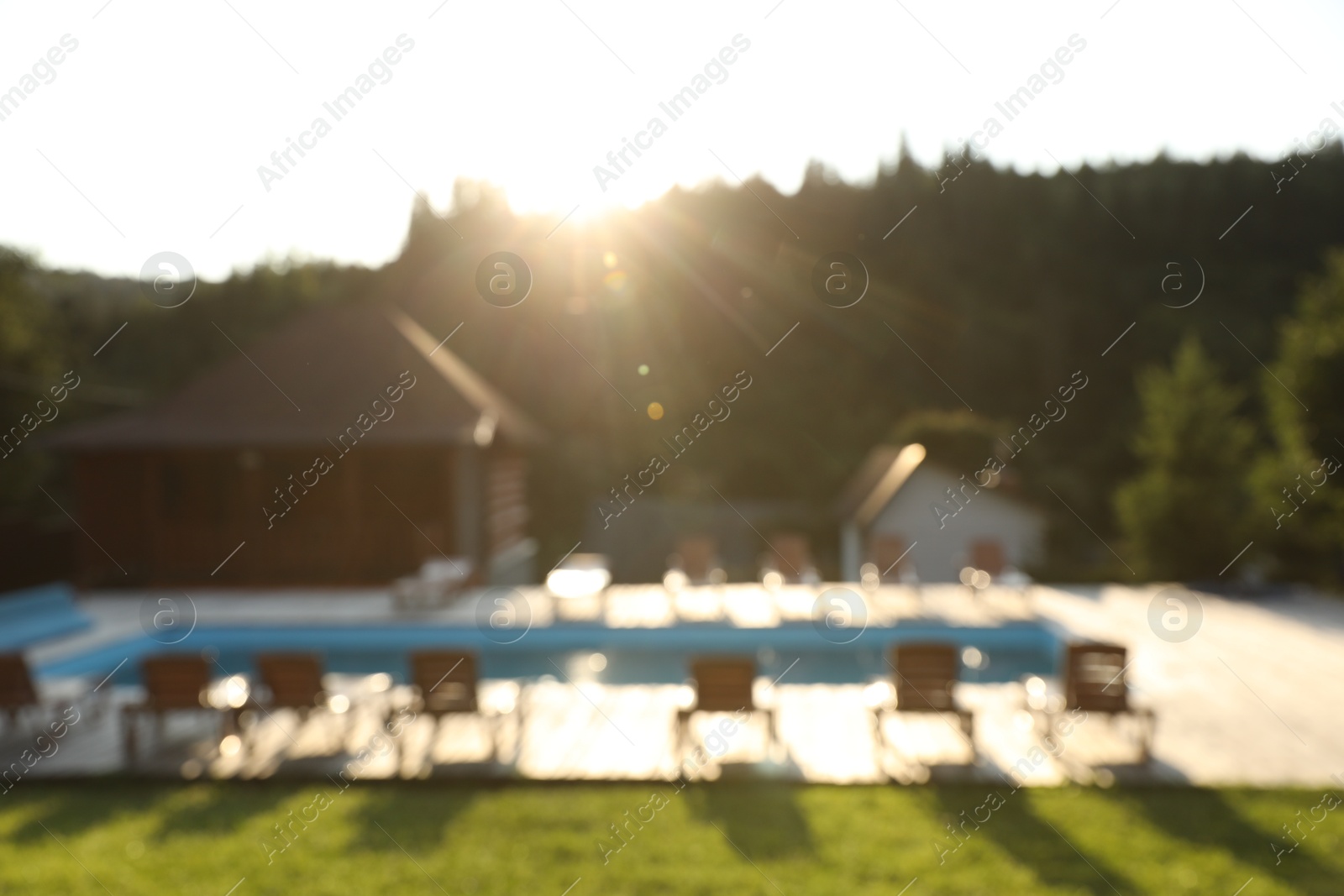 Photo of Outdoor swimming pool, sunbeds and houses near forest on sunny day, blurred view