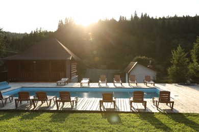 Outdoor swimming pool, sunbeds and houses near forest on sunny day