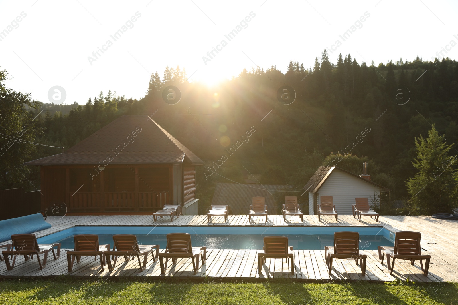 Photo of Outdoor swimming pool, sunbeds and houses near forest on sunny day