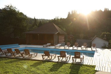 Photo of Outdoor swimming pool, sunbeds and houses near forest on sunny day