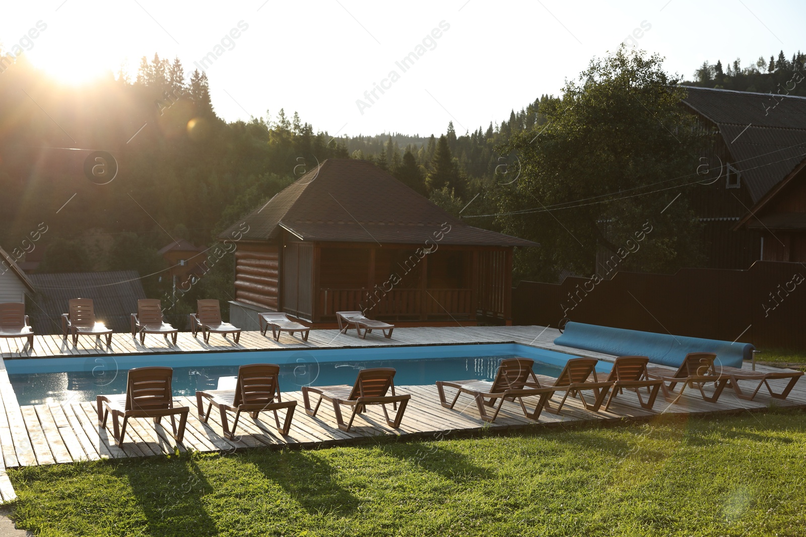 Photo of Outdoor swimming pool, sunbeds and houses near forest on sunny day