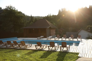 Photo of Outdoor swimming pool, sunbeds and houses near forest on sunny day