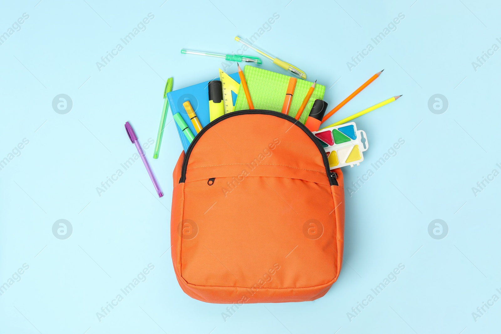 Photo of Orange backpack and different school supplies on light blue background, flat lay