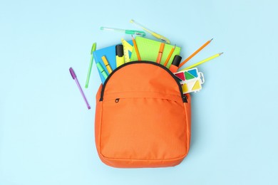 Orange backpack and different school supplies on light blue background, flat lay