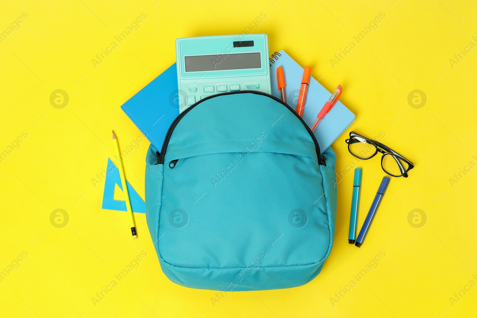 Photo of Light blue backpack and different school supplies on yellow background, flat lay