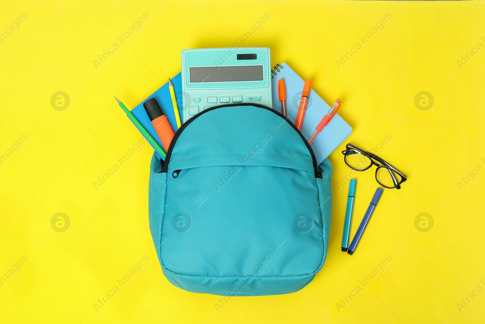 Photo of Light blue backpack and different school supplies on yellow background, flat lay