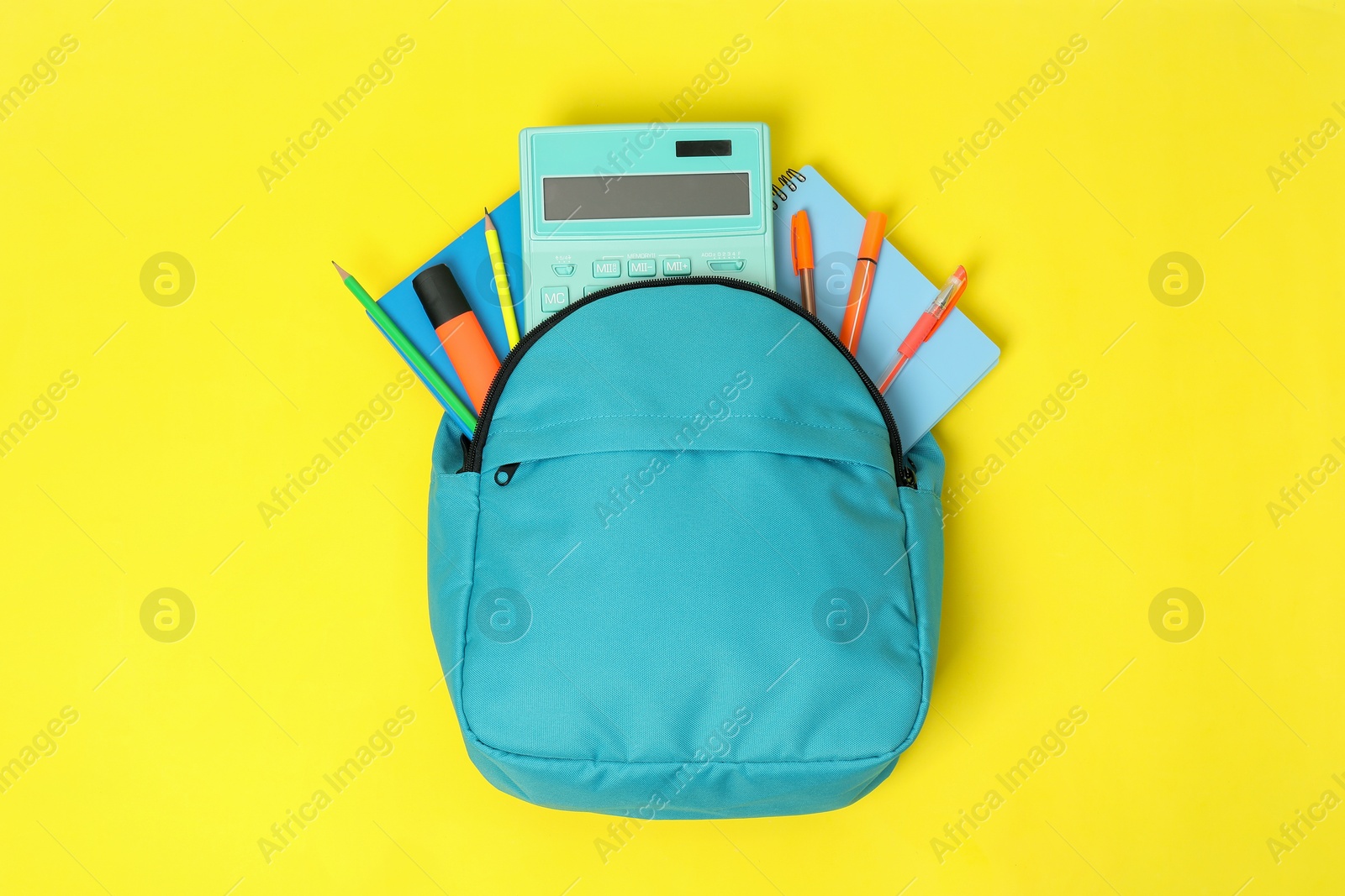 Photo of Light blue backpack with different school supplies on yellow background, top view