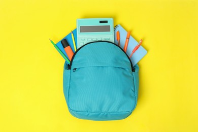 Photo of Light blue backpack with different school supplies on yellow background, top view