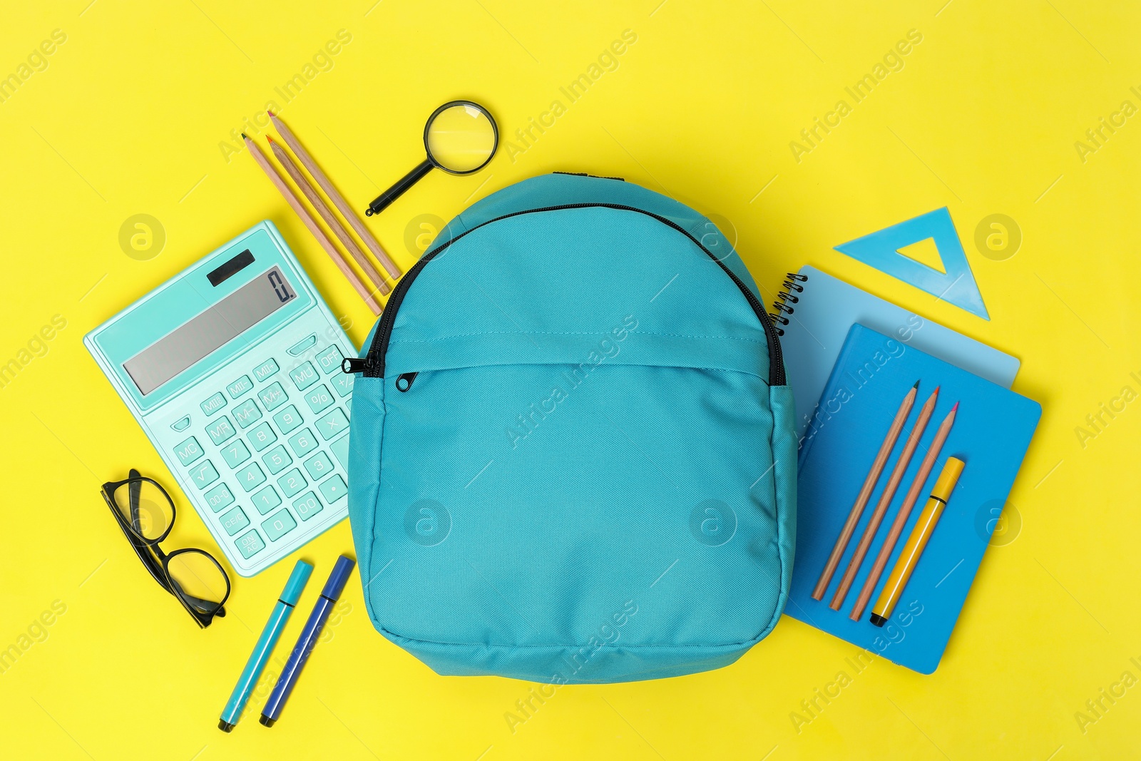 Photo of Light blue backpack and different school supplies on yellow background, flat lay