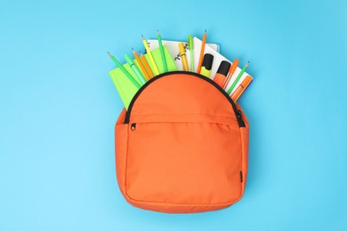 Backpack and different school supplies on light blue background, top view