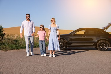 Happy family enjoying road trip. Parents and daughter near car