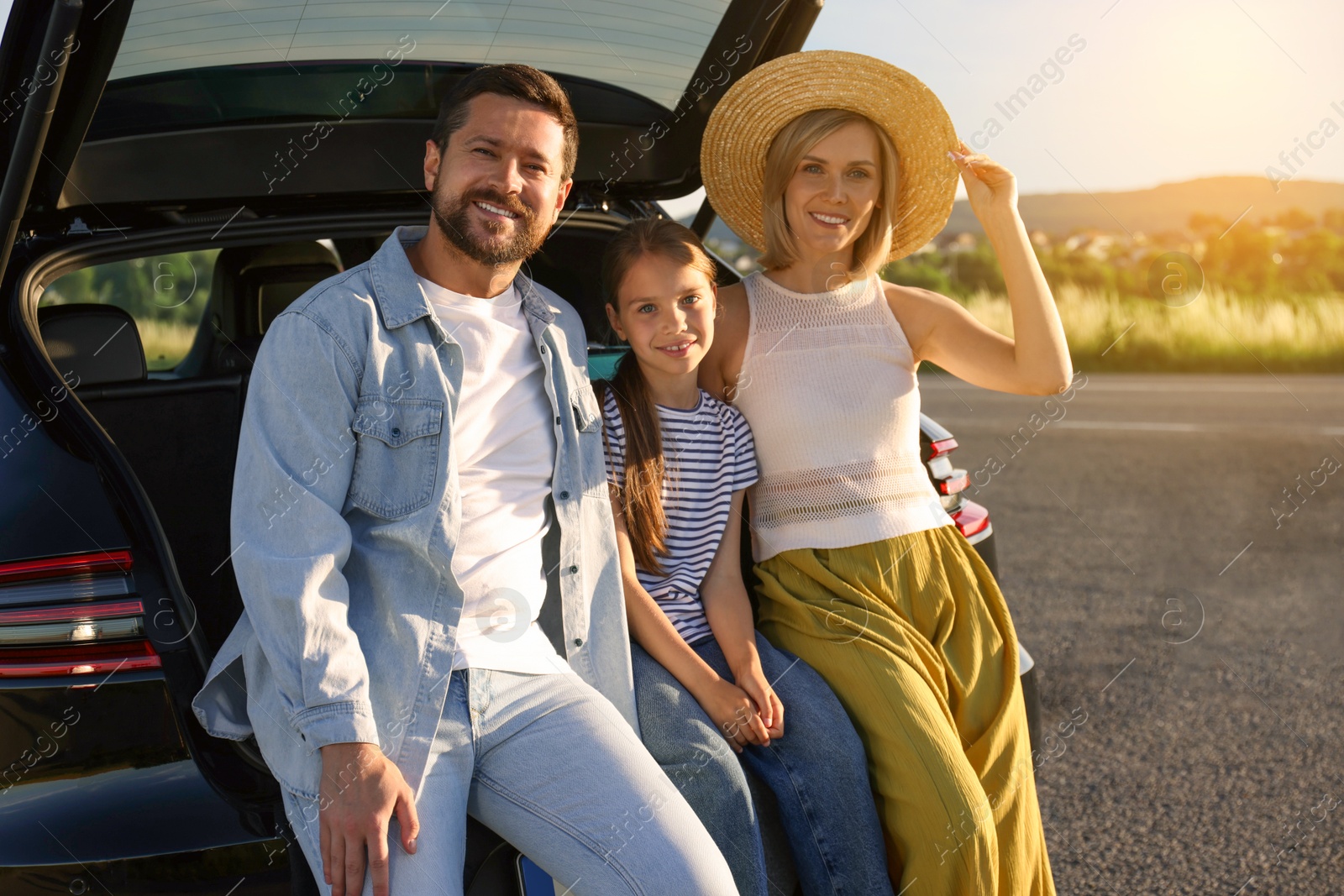 Image of Happy family enjoying road trip. Parents and daughter sitting in car trunk