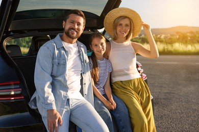 Happy family enjoying road trip. Parents and daughter sitting in car trunk