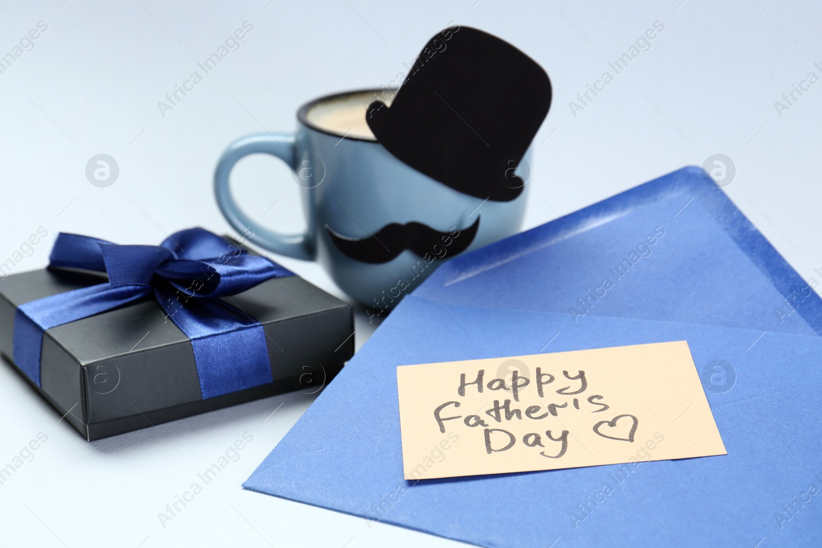 Photo of Greeting card with phrase Happy Father's Day, envelope, gift and cup of coffee on light background, closeup