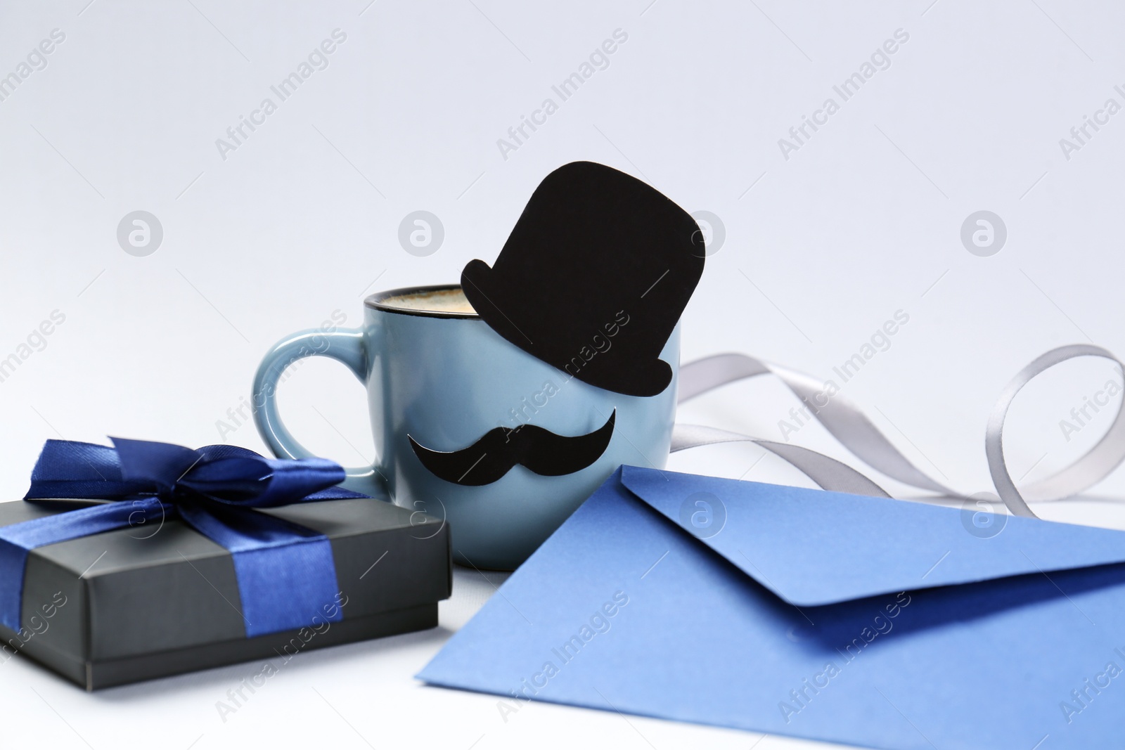 Photo of Happy Father's Day. Cup of coffee with funny paper hat, moustache, gift and envelope on light background