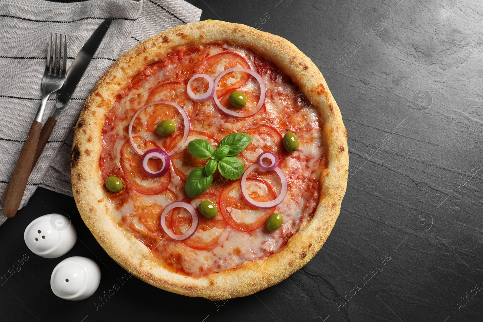 Photo of Delicious vegetarian pizza, cutlery, salt and pepper on black table, top view