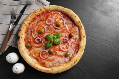 Photo of Delicious vegetarian pizza, cutlery, salt and pepper on black table, top view