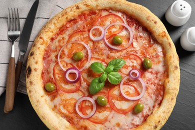 Photo of Delicious vegetarian pizza, cutlery, salt and pepper on black table, top view