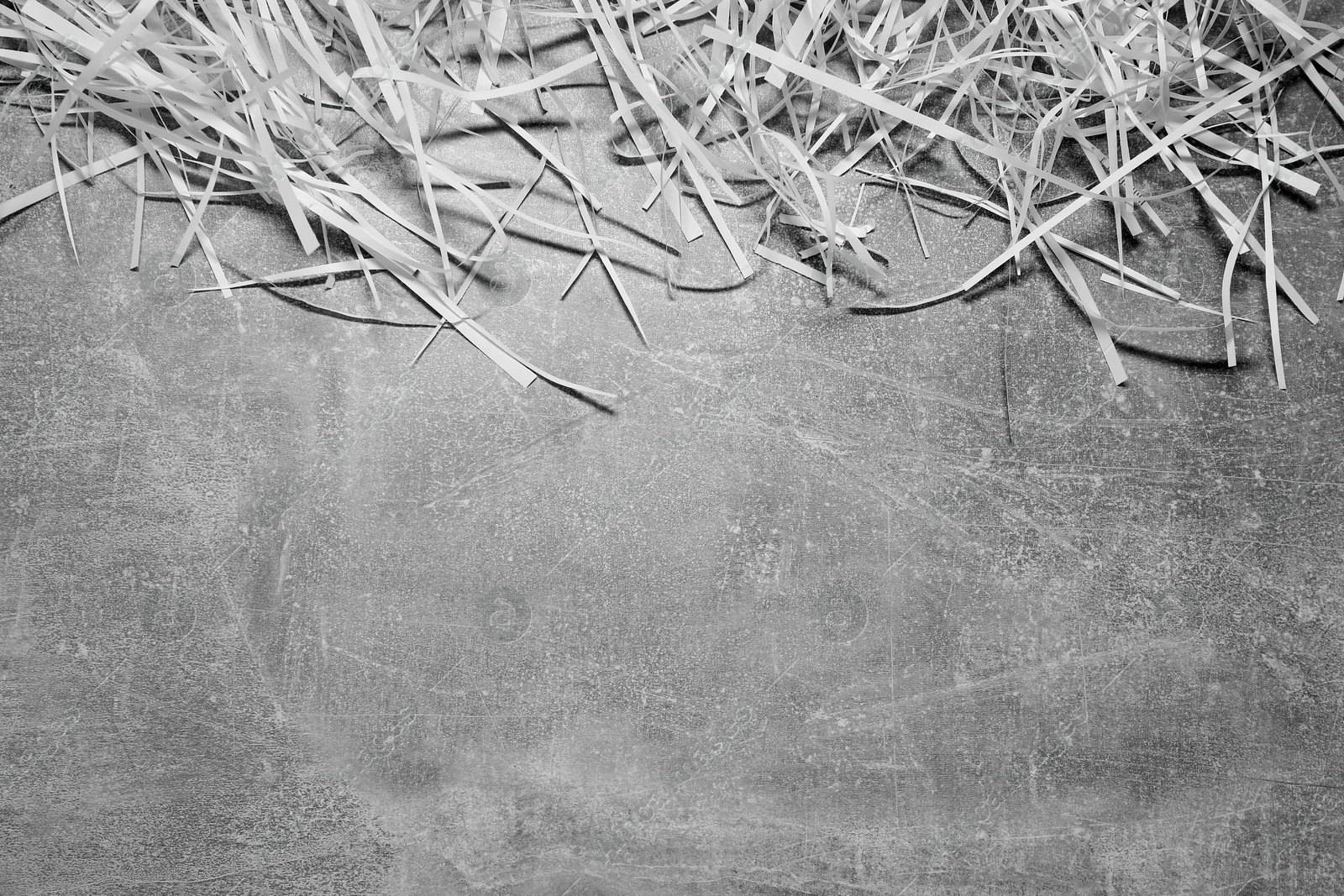 Photo of Shredded paper strips on grey textured table, top view. Space for text