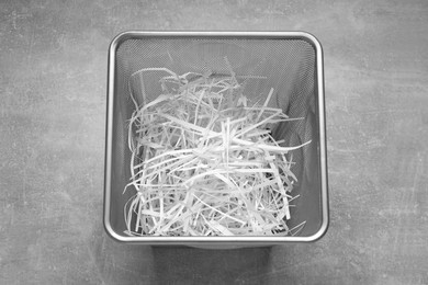 Photo of Shredded paper strips in trash bin on grey textured table, above view