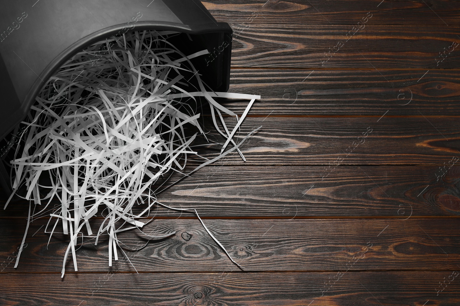 Photo of Shredded paper strips in bin on wooden table, space for text