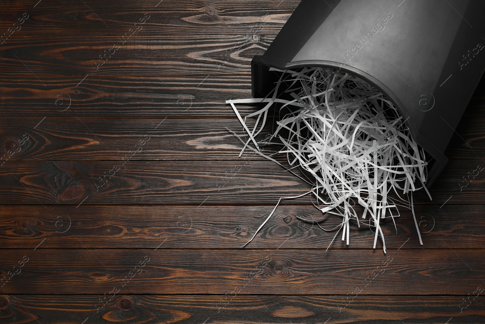 Photo of Shredded paper strips in bin on wooden table, top view. Space for text