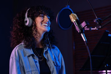 Photo of Vocalist with headphones singing into microphone in professional record studio