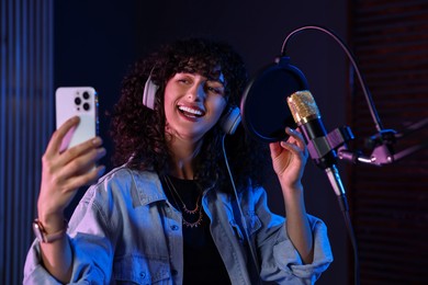 Photo of Vocalist with smartphone singing into microphone in professional record studio