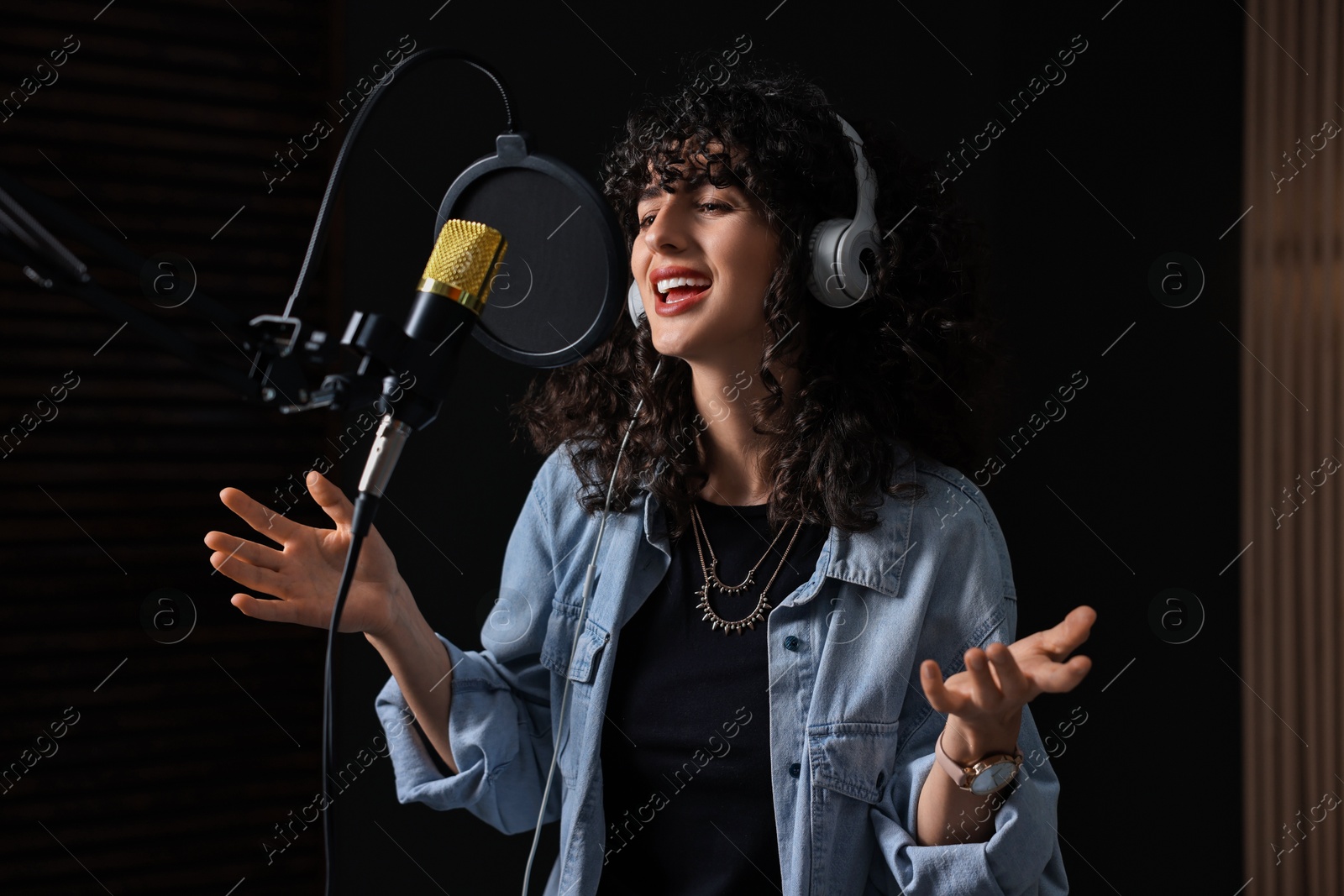 Photo of Vocalist with headphones singing into microphone in professional record studio