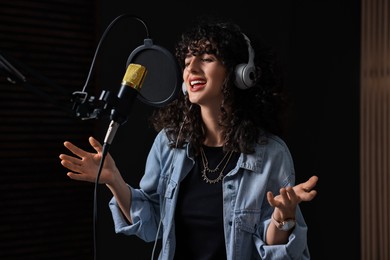 Photo of Vocalist with headphones singing into microphone in professional record studio