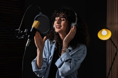 Photo of Vocalist with headphones singing into microphone in professional record studio