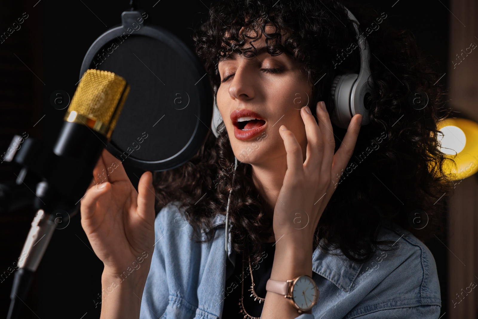 Photo of Vocalist with headphones singing into microphone in professional record studio