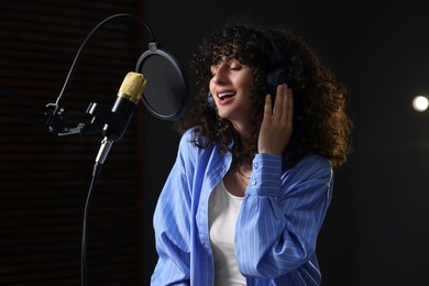 Photo of Vocalist with headphones singing into microphone in professional record studio