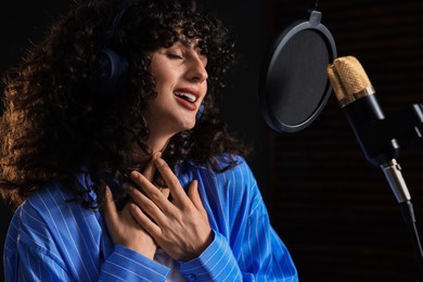 Photo of Vocalist with headphones singing into microphone in professional record studio