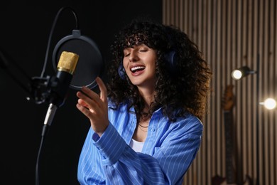 Photo of Vocalist with headphones singing into microphone in professional record studio