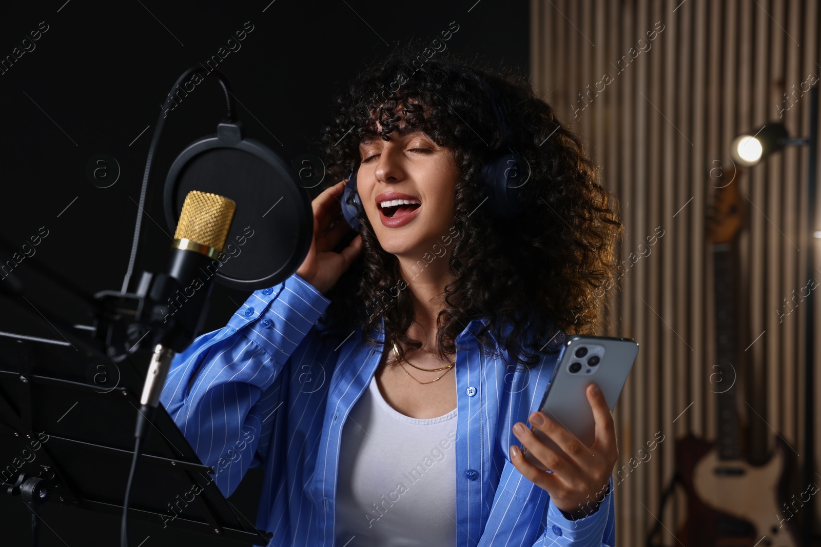 Photo of Vocalist with smartphone singing into microphone in professional record studio