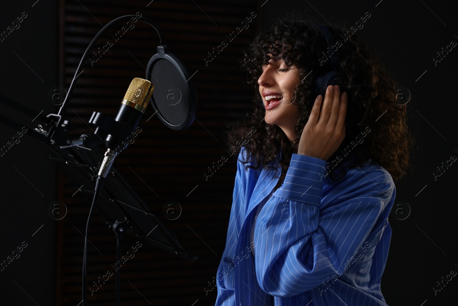 Photo of Vocalist with headphones singing into microphone in professional record studio