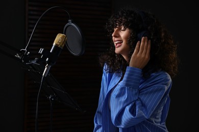 Photo of Vocalist with headphones singing into microphone in professional record studio