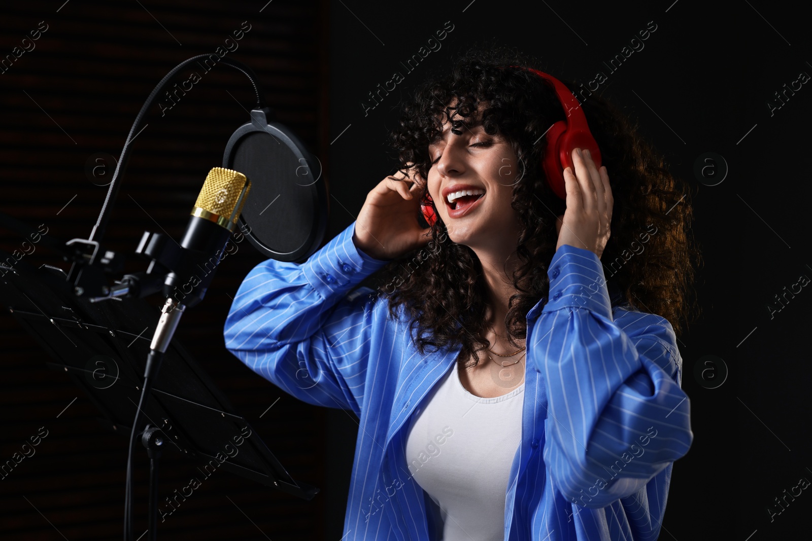 Photo of Vocalist with headphones singing into microphone in professional record studio